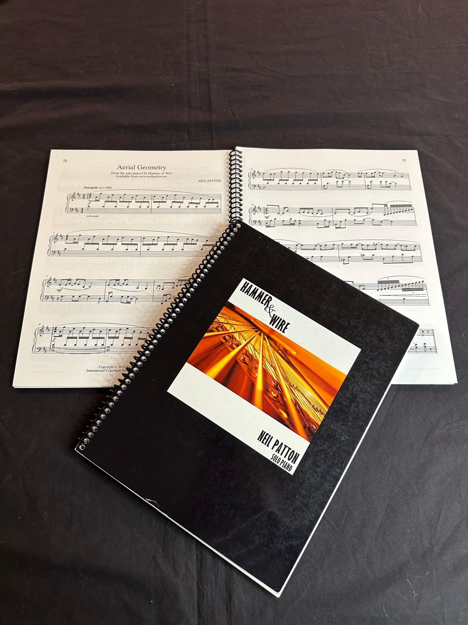 A closed copy of the Hammer & Wire songbook lying on another open copy of the book, displaying a sample of the printed music inside.