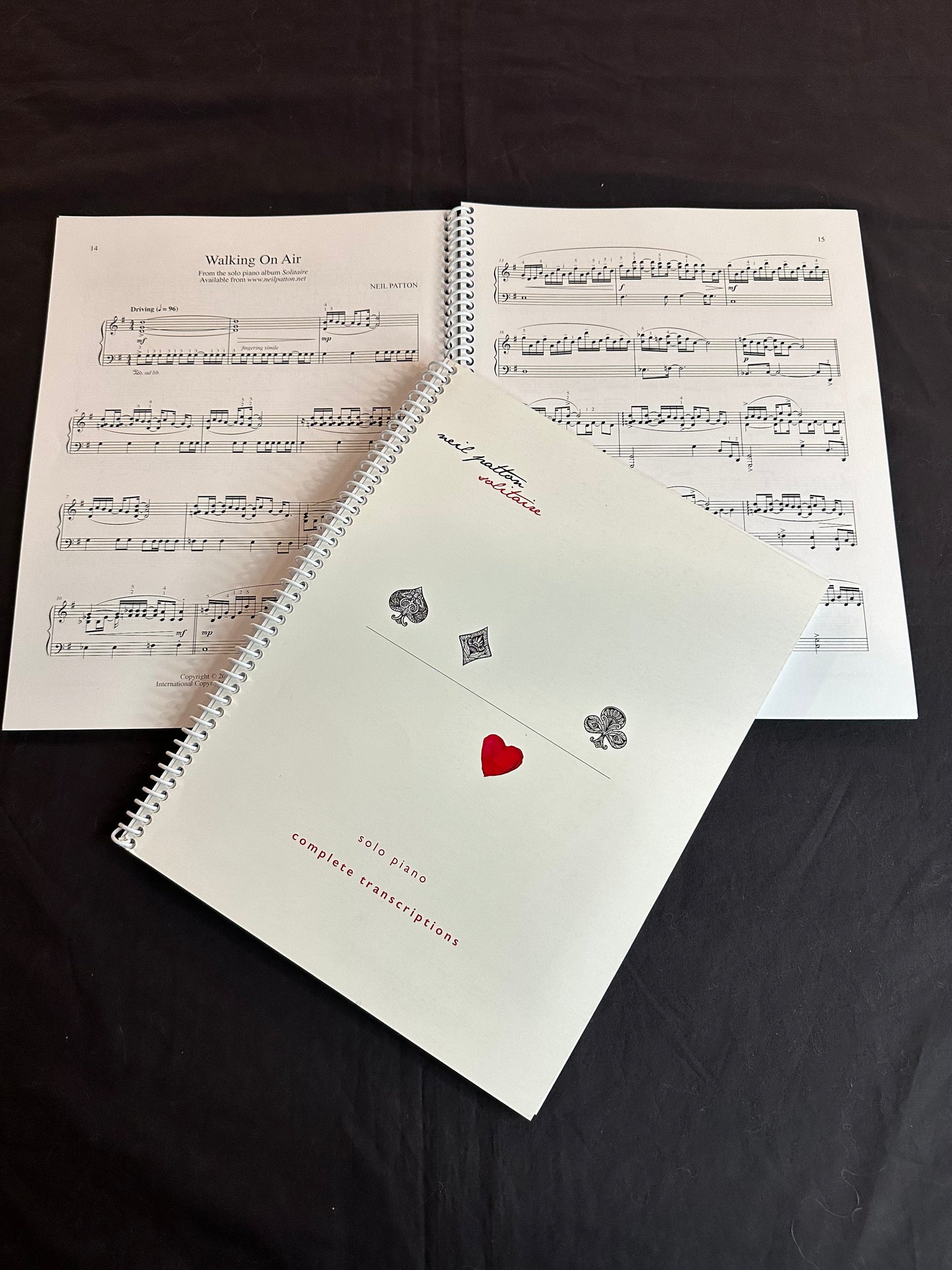 A closed copy of the Solitaire Songbook lying on another open copy, displaying a sample of the printed music inside.