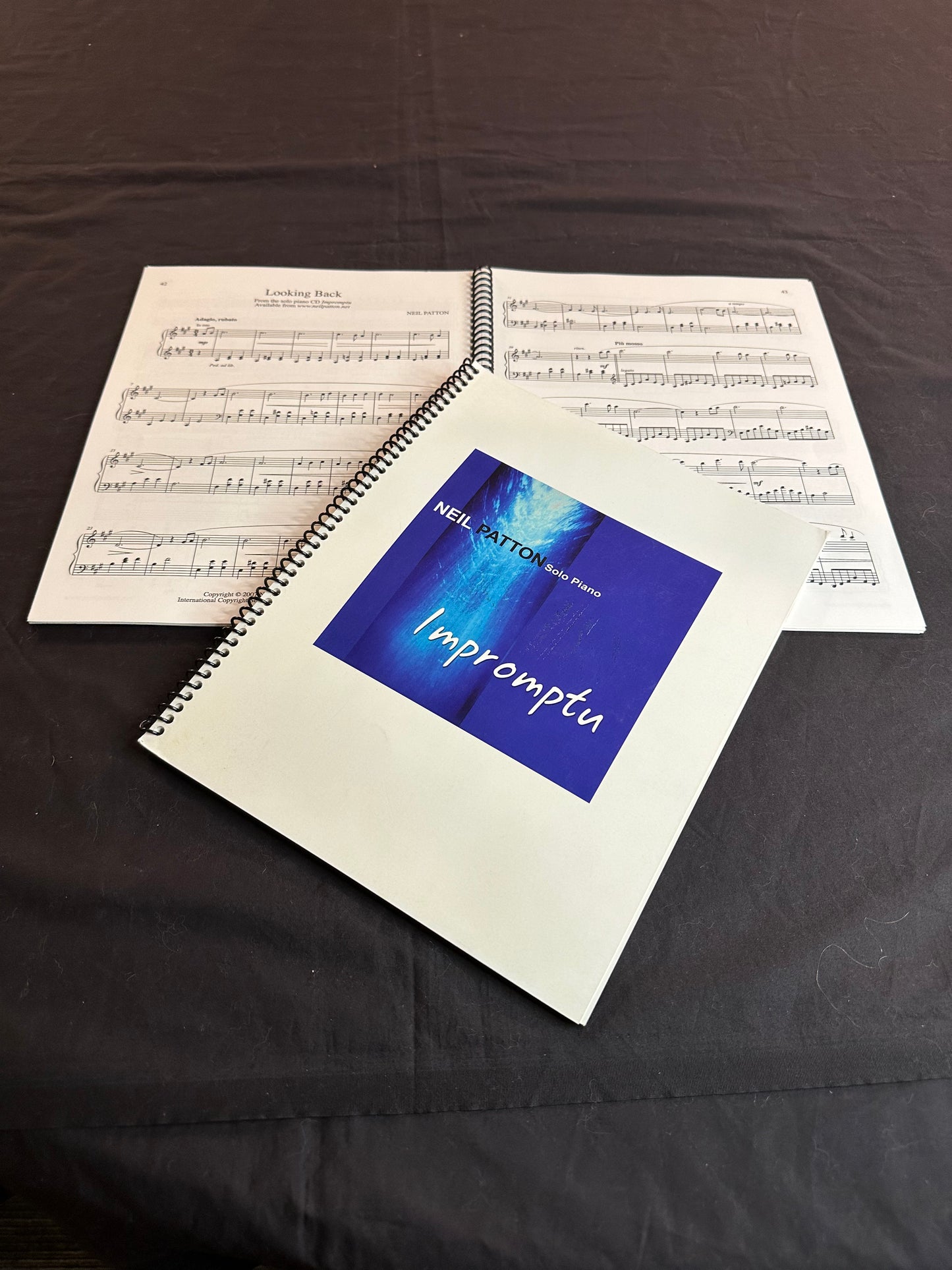 A closed copy of the Impromptu Songbook lying on another open copy displaying some of the printed music inside.